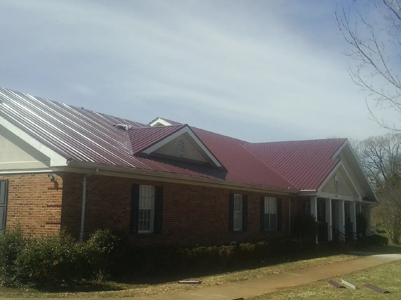 Red metal roof with gabled entries on a long brick building, from a Hail Damage Roof Repair job in Pocatello