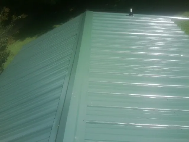 New green metal panels meeting at the ridge of a roof — Flat Roof Repair work by our crew in Pocatello