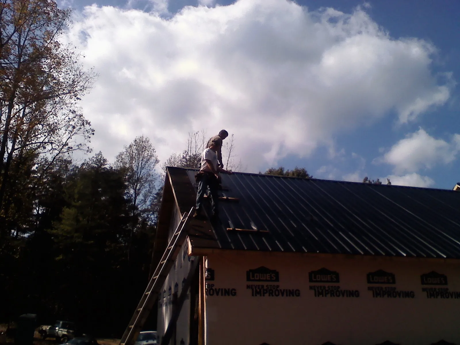 Roofer fastening dark metal panels high against a cloudy sky, from a Roof Inspection job in Pocatello