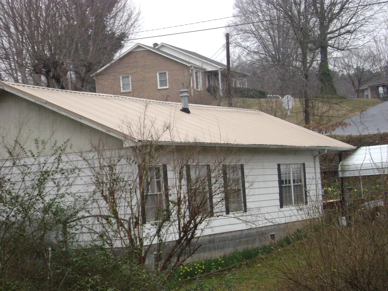 Tan metal roof on a white sided house set into a hillside — Commercial Roofing by Roofing Brothers in Pocatello